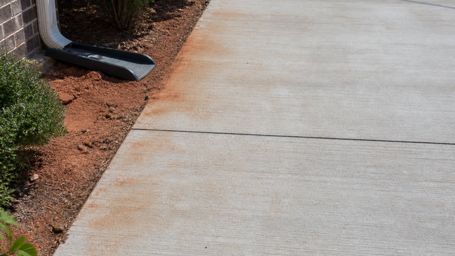 Concrete driveway with a saw-cut joint and rust-red clay staining near a bed